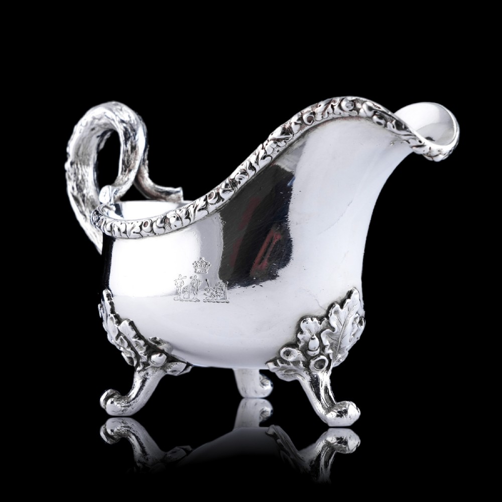 A Victorian sterling silver sauce boat featuring an organic twig handle, acorn feet, and engraved crest detailing. View VI