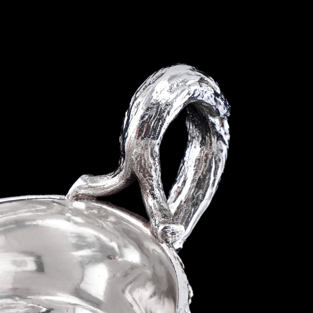 A Victorian sterling silver sauce boat featuring an organic twig handle, acorn feet, and engraved crest detailing. View VIII