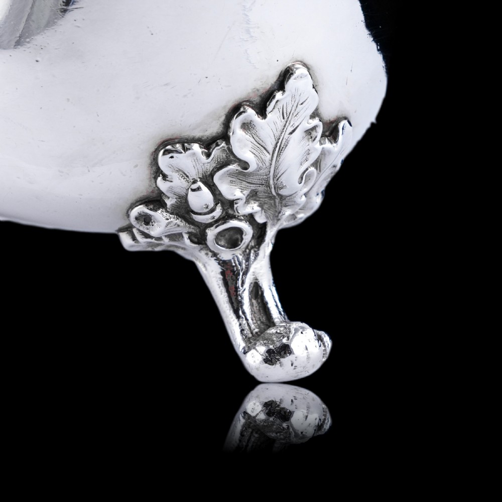 A Victorian sterling silver sauce boat featuring an organic twig handle, acorn feet, and engraved crest detailing. View X