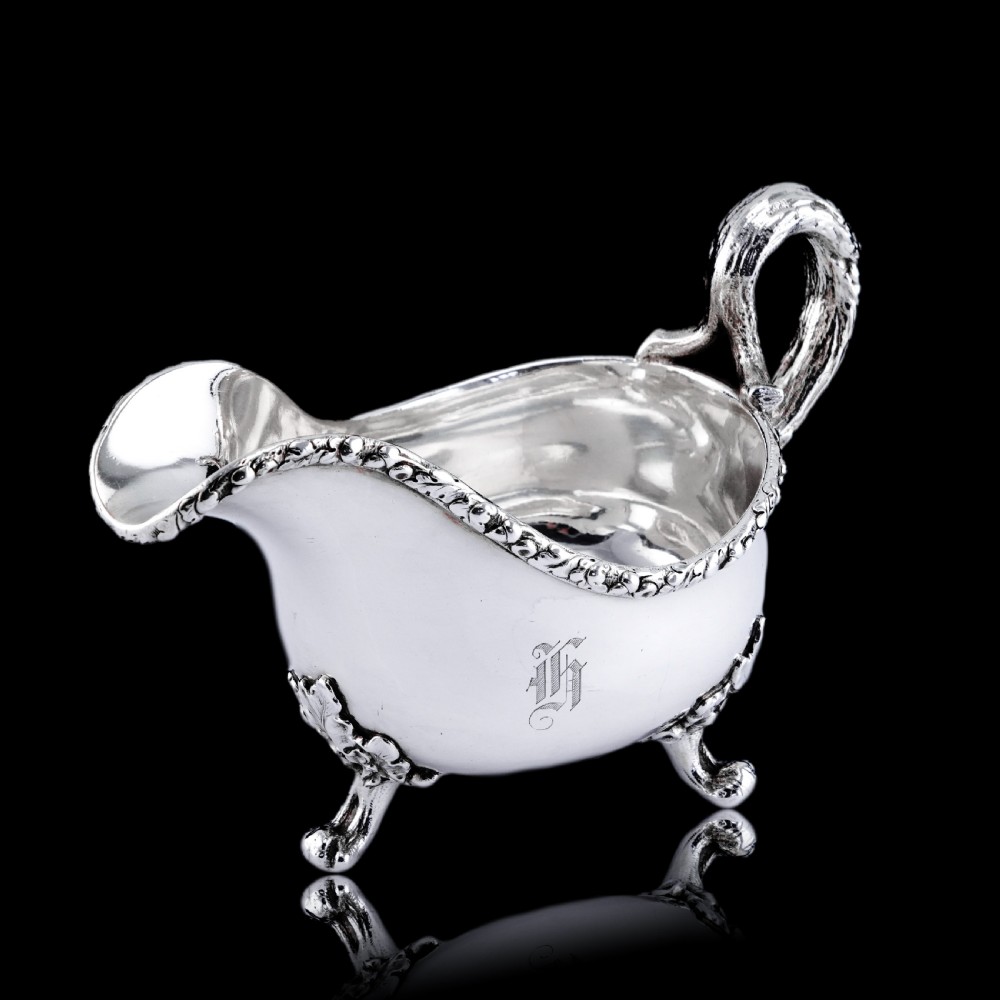 A Victorian sterling silver sauce boat featuring an organic twig handle, acorn feet, and engraved crest detailing. View XVI