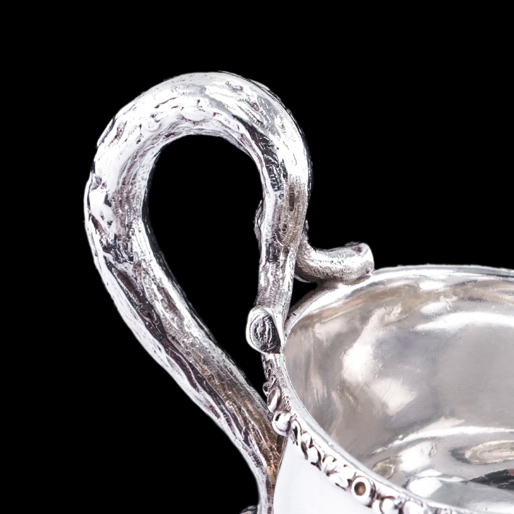 A Victorian sterling silver sauce boat featuring an organic twig handle, acorn feet, and engraved crest detailing. View XX