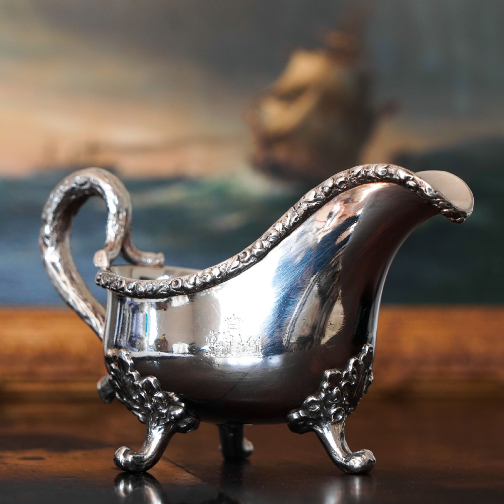 A Victorian sterling silver sauce boat featuring acorn and leaf feet, a branch-formed handle, and an engraved crest.