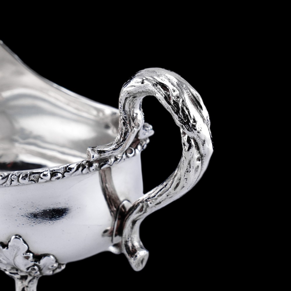 A Victorian sterling silver sauce boat featuring acorn and leaf feet, a branch-formed handle, and an engraved crest. View XVII