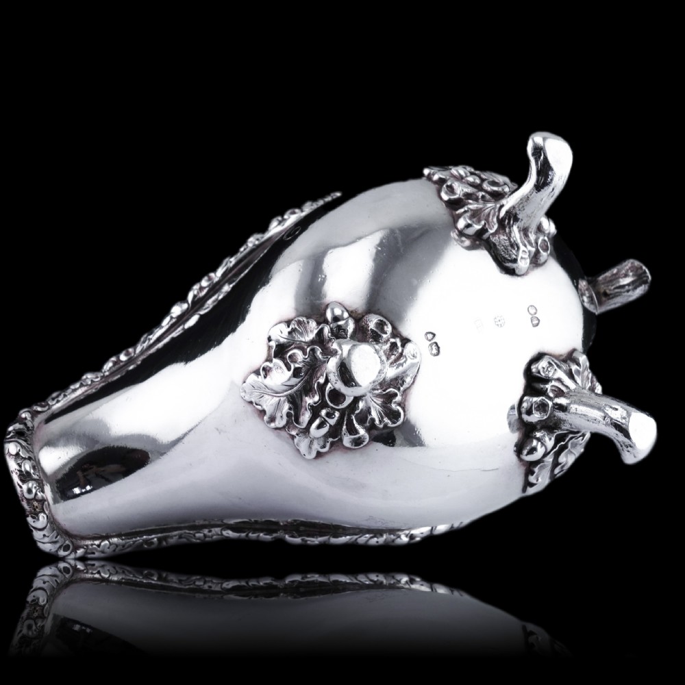 A Victorian sterling silver sauce boat featuring acorn and leaf feet, a branch-formed handle, and an engraved crest. View XXI