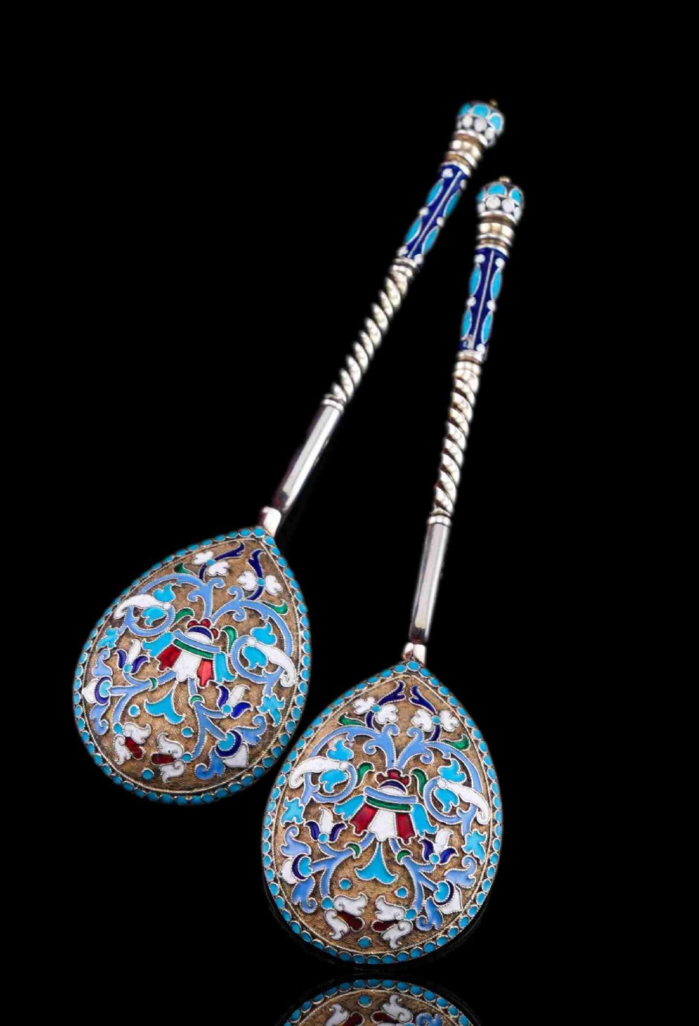 A pair of late 19th-century Russian solid silver spoons featuring turquoise, blue, and white cloisonne enamel foliate decoration on silver-gilt teardrop bowls with twisted handles.