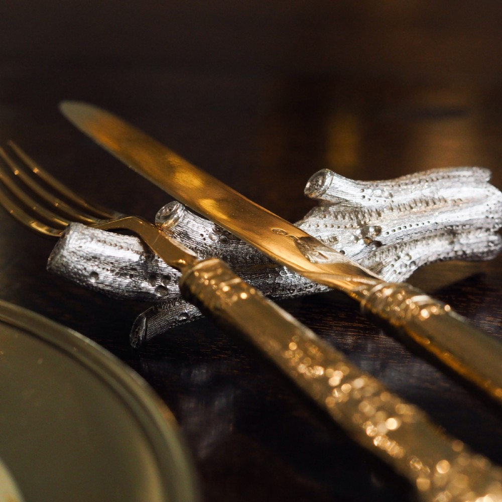 A detailed close-up of a Victorian solid silver knife rest fashioned in the shape of a textured tree branch. View II