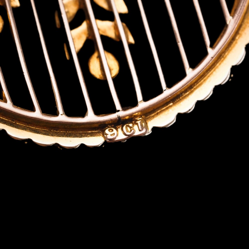 An Edwardian circular gold pendant featuring a halo of seed pearls framing an inner wire grid with a pearl-set floral garland and a central round pink tourmaline. View XI