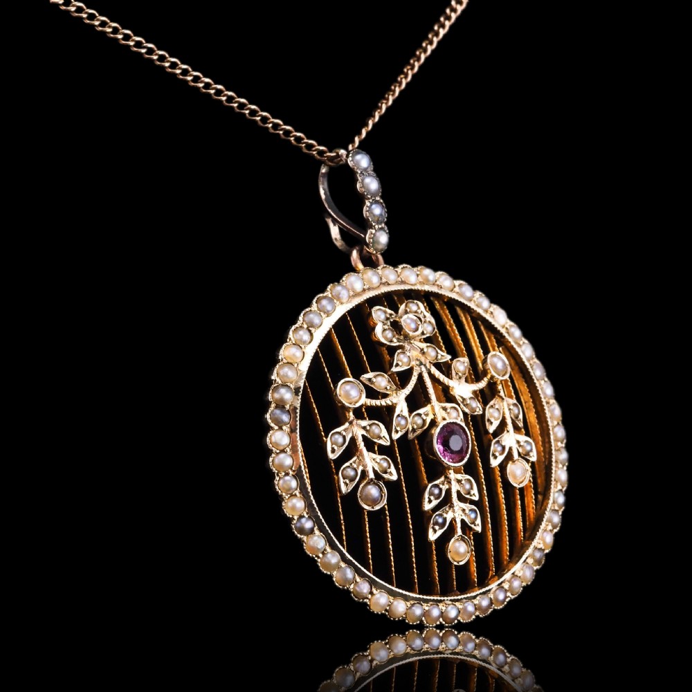 An Edwardian circular gold pendant featuring a halo of seed pearls framing an inner wire grid with a pearl-set floral garland and a central round pink tourmaline. View XIV