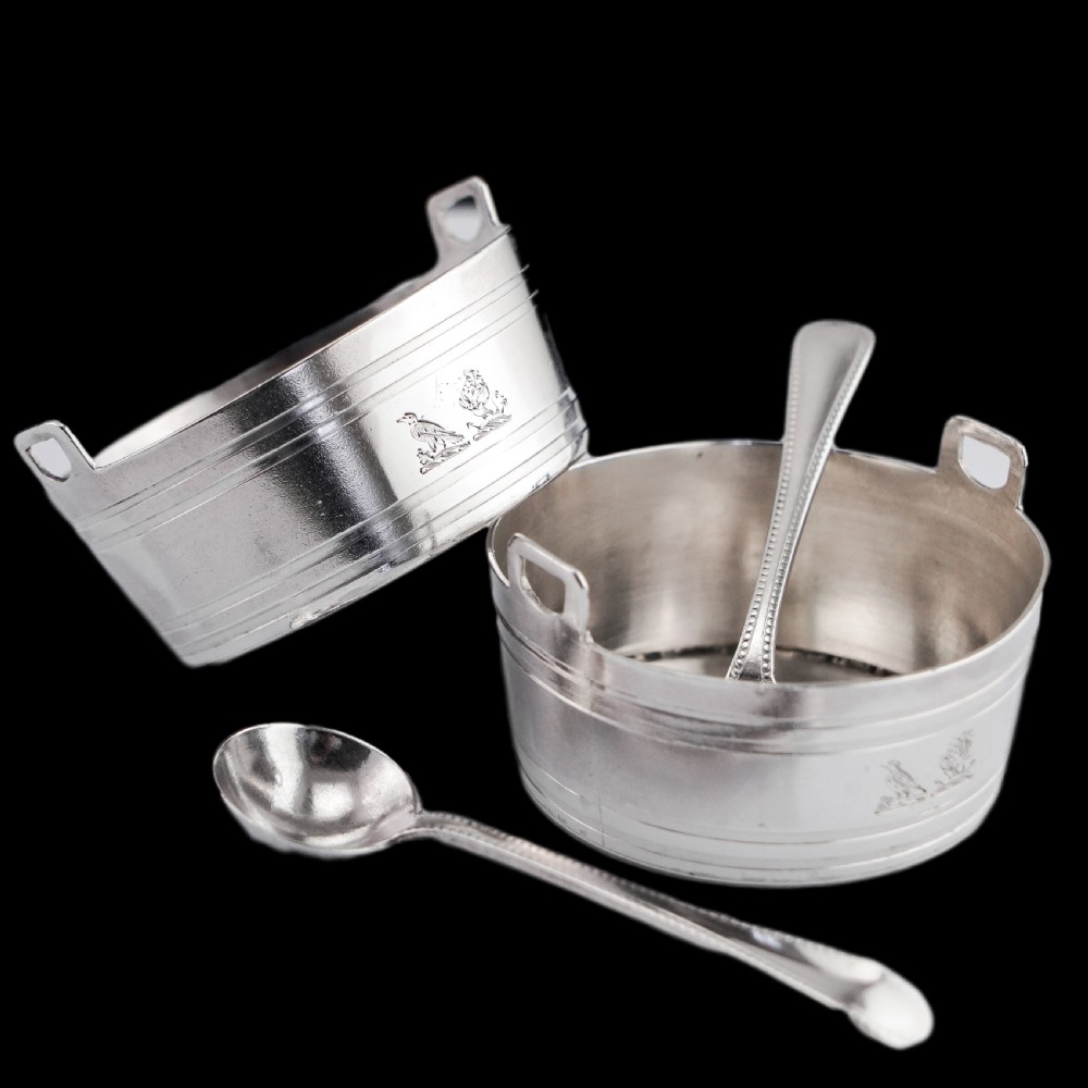 A pair of Victorian solid silver salt cellars crafted in the form of small pails with handles and engraved bird motifs, shown alongside two matching silver spoons. View II