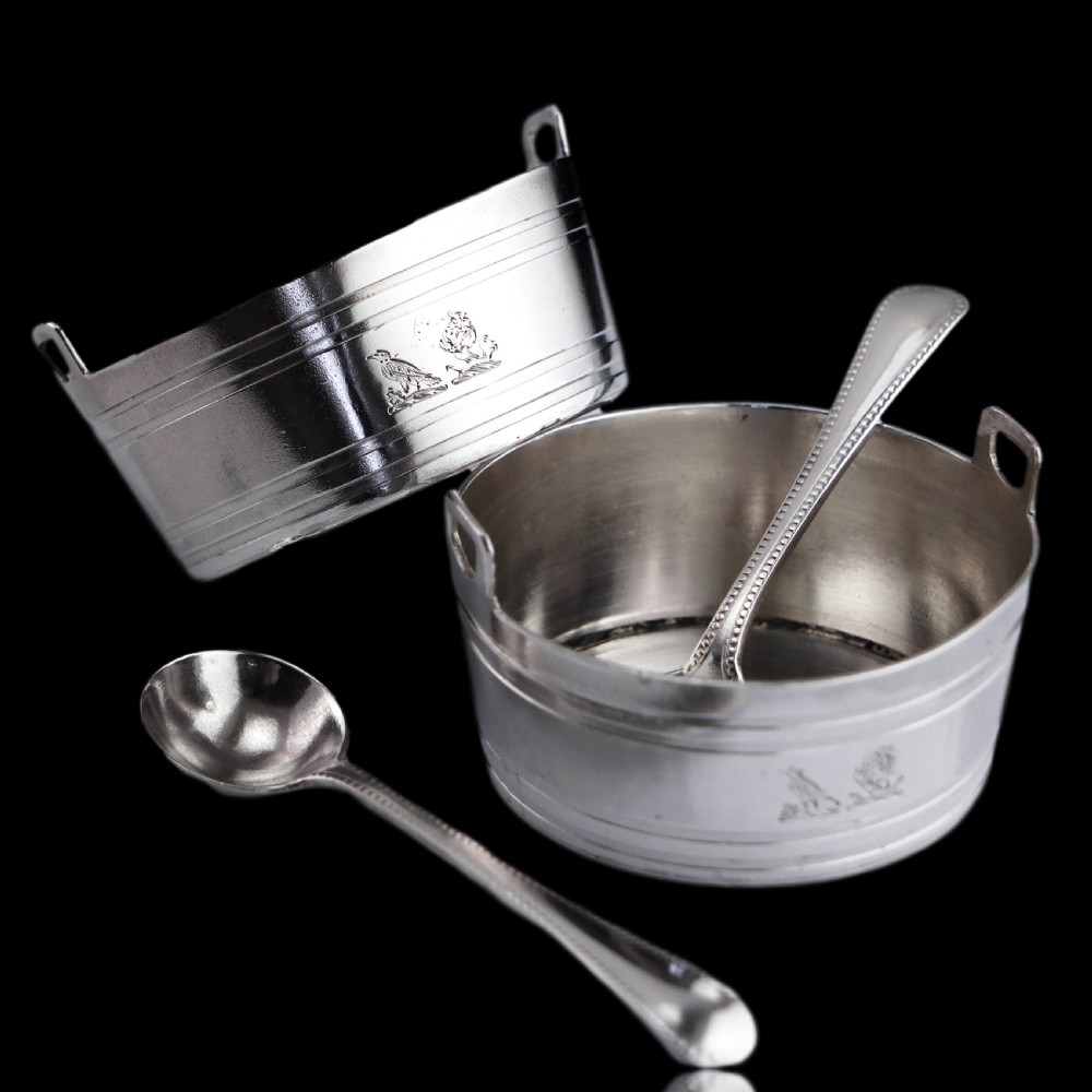 A pair of Victorian solid silver salt cellars crafted in the form of small pails with handles and engraved bird motifs, shown alongside two matching silver spoons. View III