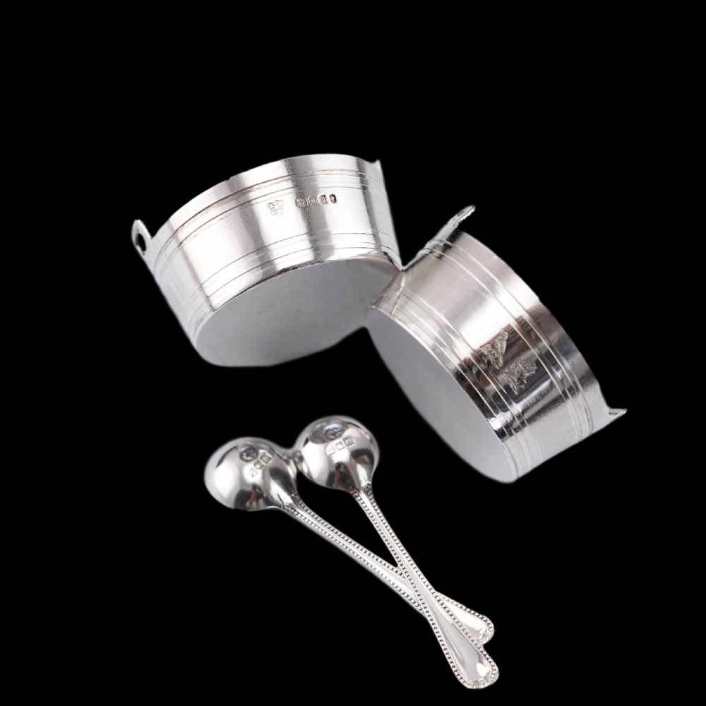 A pair of Victorian solid silver salt cellars crafted in the form of small pails with handles and engraved bird motifs, shown alongside two matching silver spoons. View VI