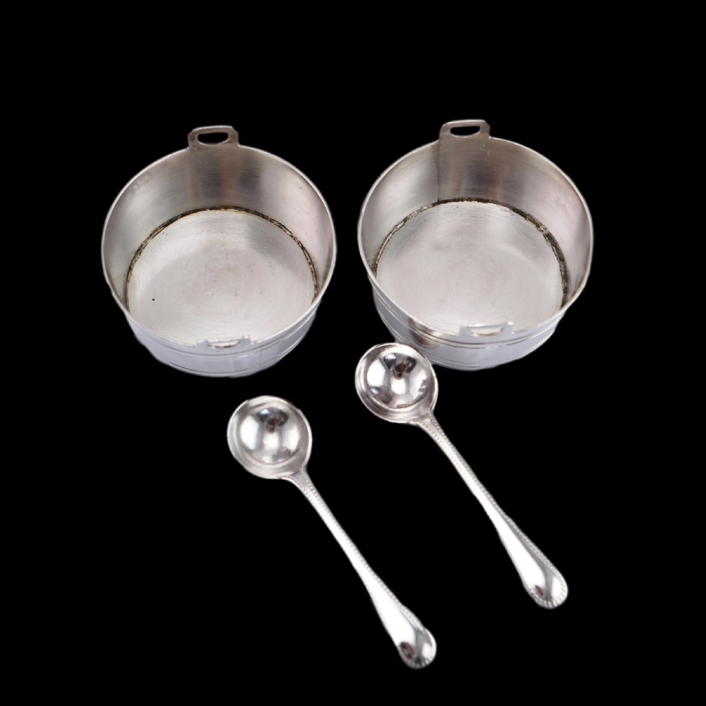 A pair of Victorian solid silver salt cellars crafted in the form of small pails with handles and engraved bird motifs, shown alongside two matching silver spoons. View VII
