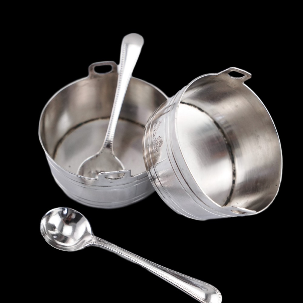 A pair of Victorian solid silver salt cellars crafted in the form of small pails with handles and engraved bird motifs, shown alongside two matching silver spoons. View VIII