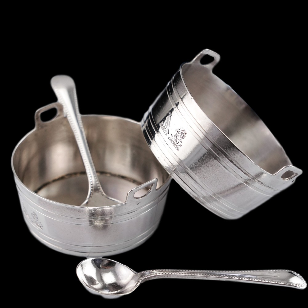 A pair of Victorian solid silver salt cellars crafted in the form of small pails with handles and engraved bird motifs, shown alongside two matching silver spoons. View IX