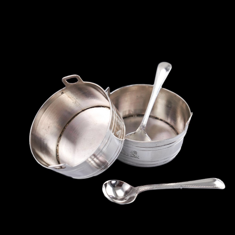 A pair of Victorian solid silver salt cellars crafted in the form of small pails with handles and engraved bird motifs, shown alongside two matching silver spoons. View XI