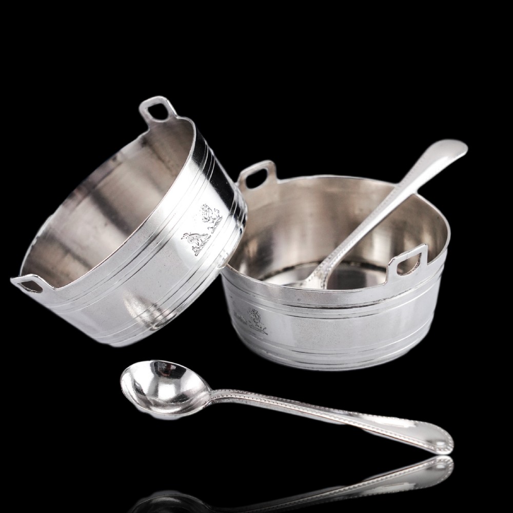 A pair of Victorian solid silver salt cellars crafted in the form of small pails with handles and engraved bird motifs, shown alongside two matching silver spoons. View XII
