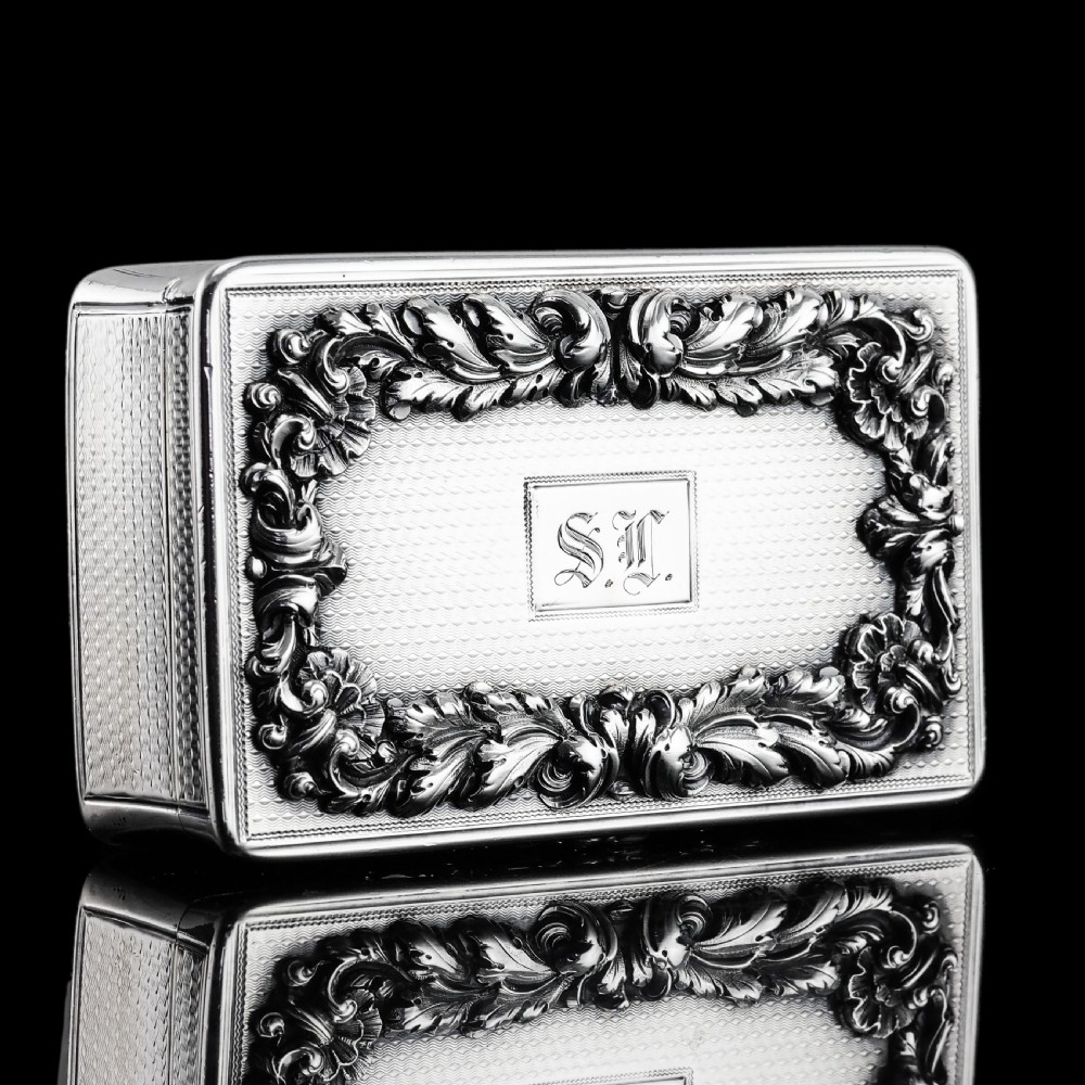 A rectangular Victorian sterling silver snuff box with an open hinged lid, engine-turned engraving, cast acanthus leaf border, and a gilt interior. View V