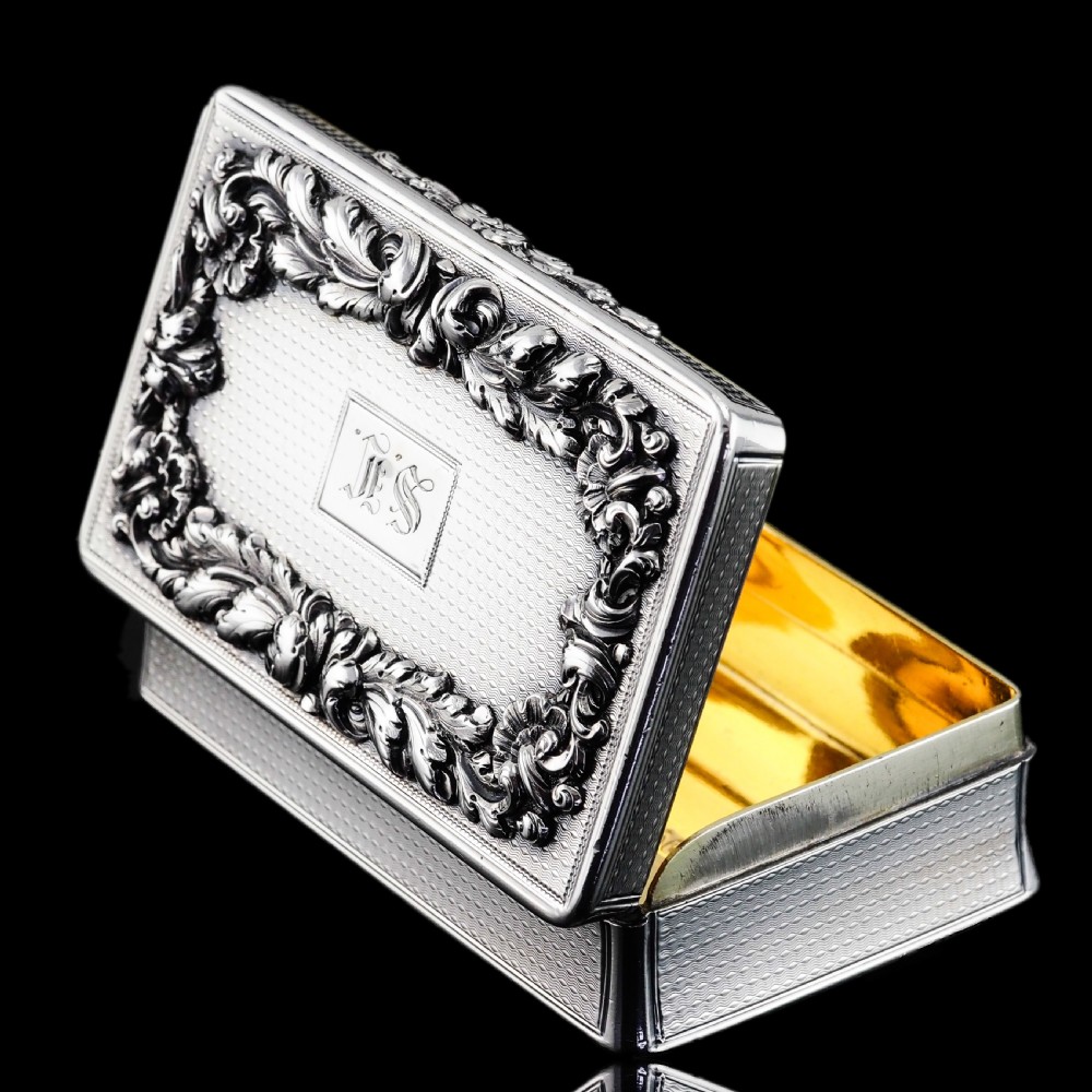 A rectangular Victorian sterling silver snuff box with an open hinged lid, engine-turned engraving, cast acanthus leaf border, and a gilt interior. View VI