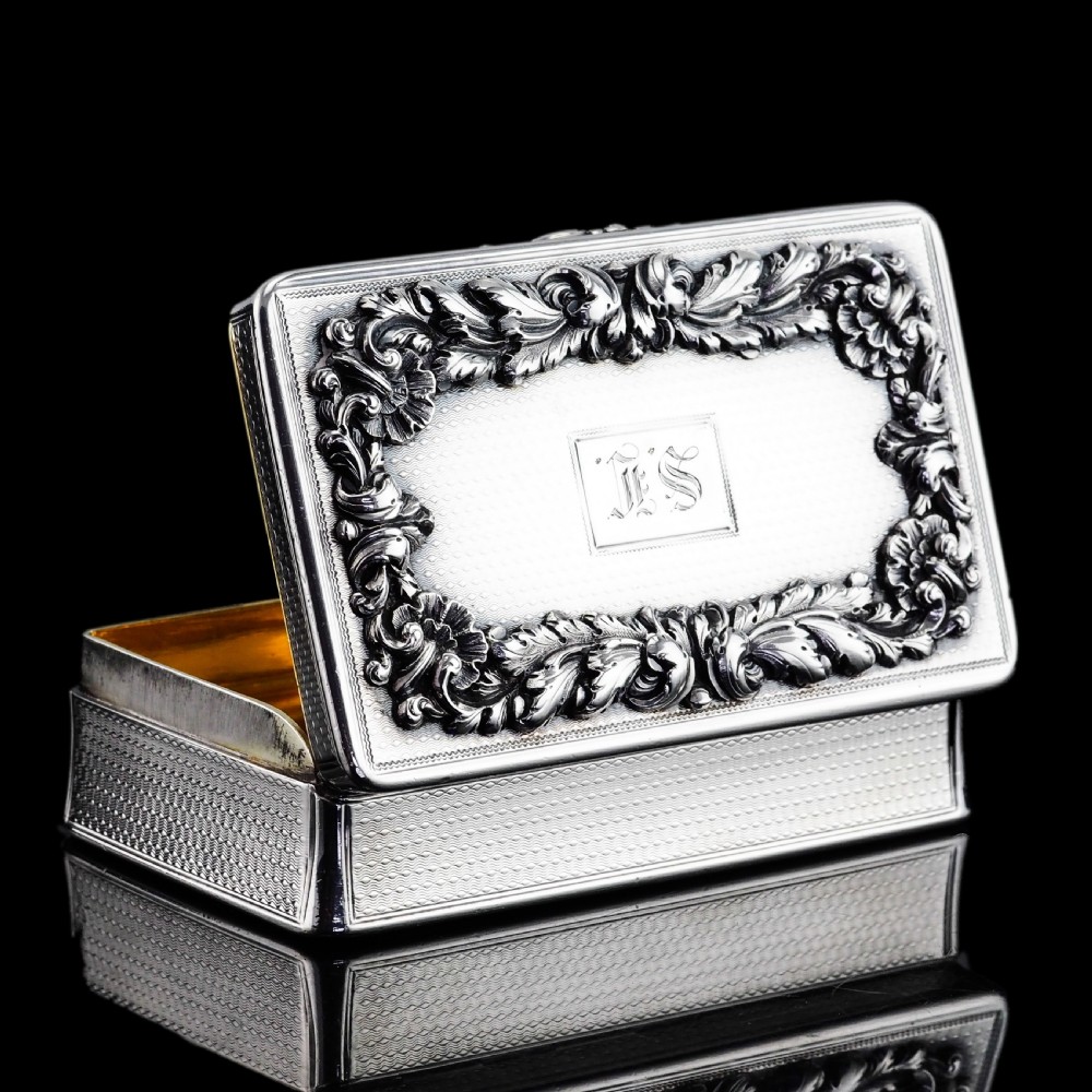 A rectangular Victorian sterling silver snuff box with an open hinged lid, engine-turned engraving, cast acanthus leaf border, and a gilt interior. View VII