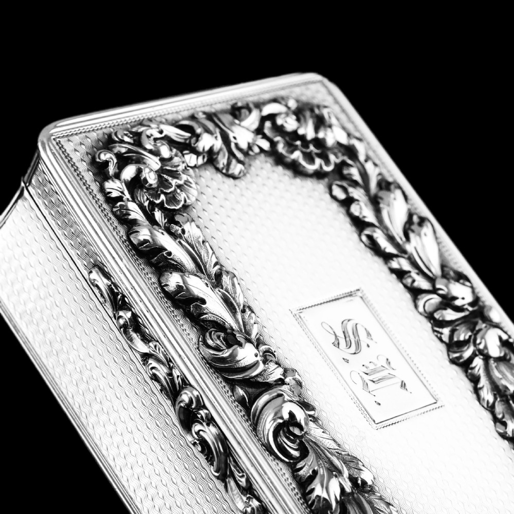 A rectangular Victorian sterling silver snuff box with an open hinged lid, engine-turned engraving, cast acanthus leaf border, and a gilt interior. View X