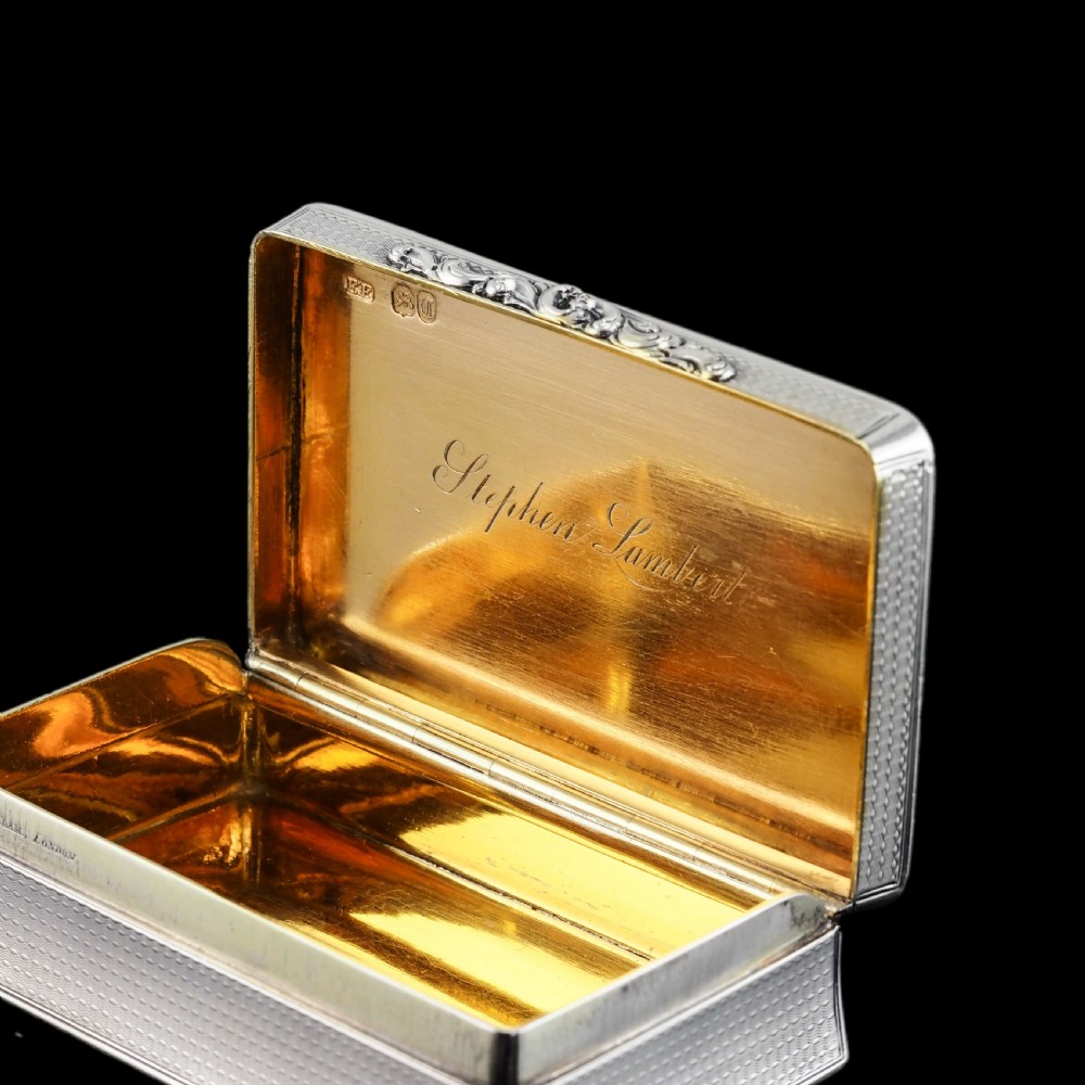 A rectangular Victorian sterling silver snuff box with an open hinged lid, engine-turned engraving, cast acanthus leaf border, and a gilt interior. View XI