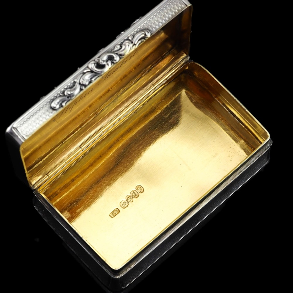 A rectangular Victorian sterling silver snuff box with an open hinged lid, engine-turned engraving, cast acanthus leaf border, and a gilt interior. View XVII
