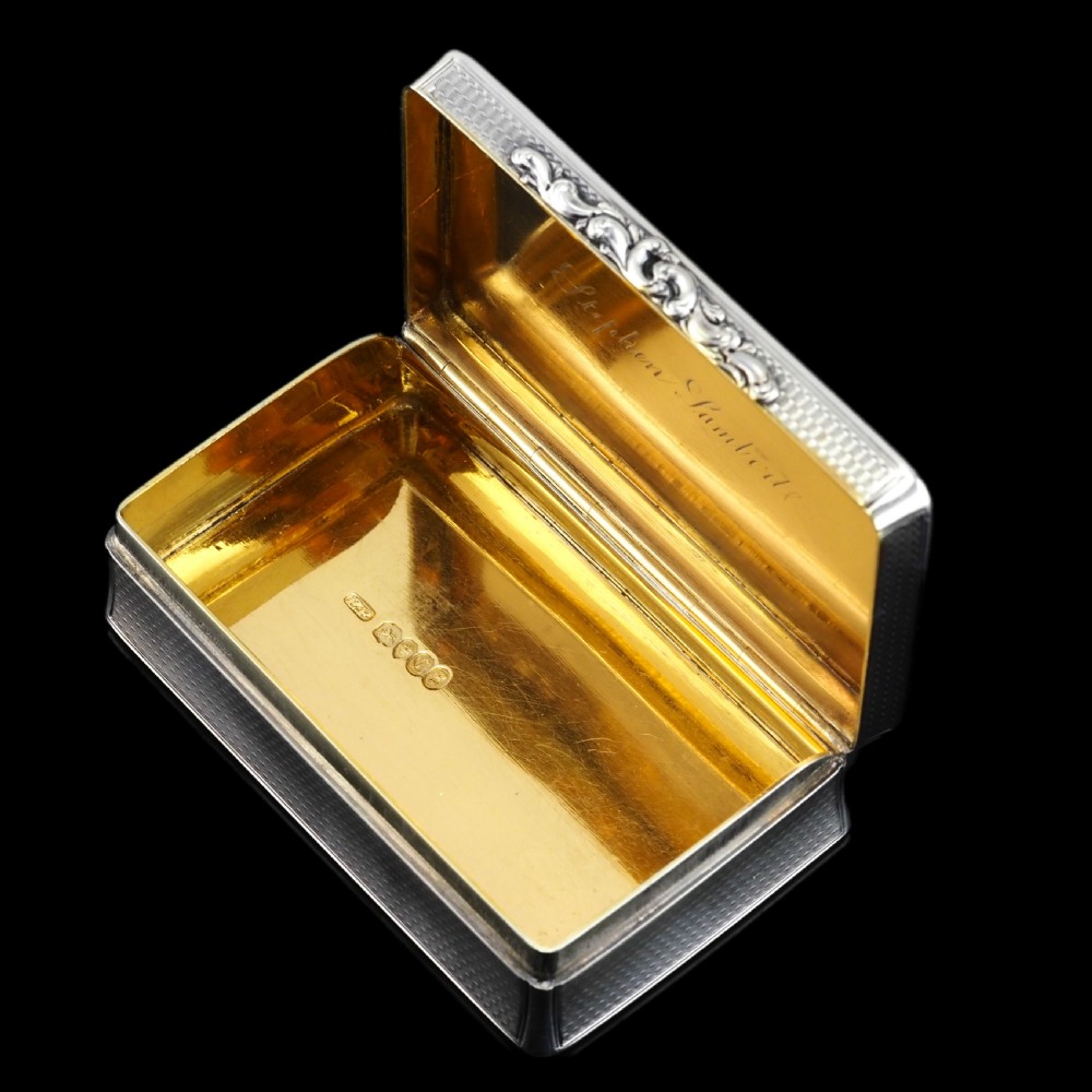 A rectangular Victorian sterling silver snuff box with an open hinged lid, engine-turned engraving, cast acanthus leaf border, and a gilt interior. View XVIII