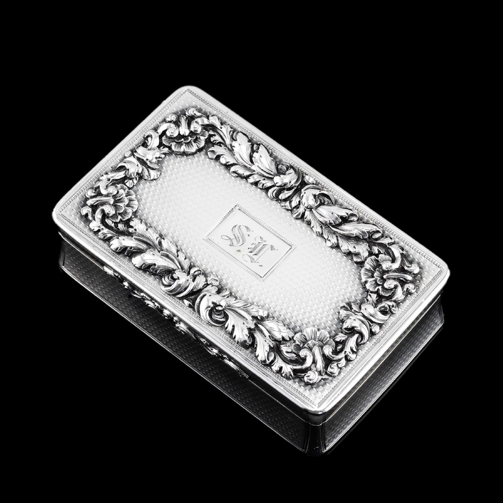 A rectangular Victorian sterling silver snuff box with an open hinged lid, engine-turned engraving, cast acanthus leaf border, and a gilt interior. View XX