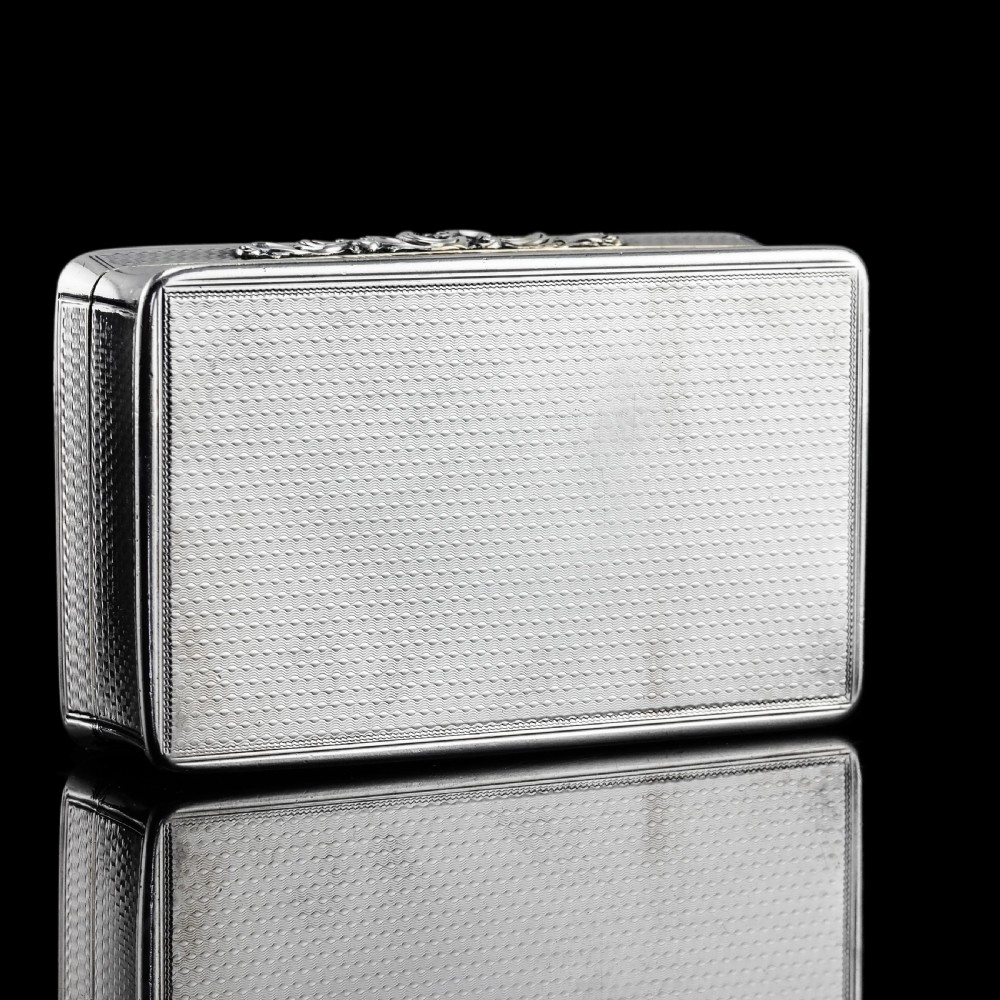 A rectangular Victorian sterling silver snuff box with an open hinged lid, engine-turned engraving, cast acanthus leaf border, and a gilt interior. View XXII