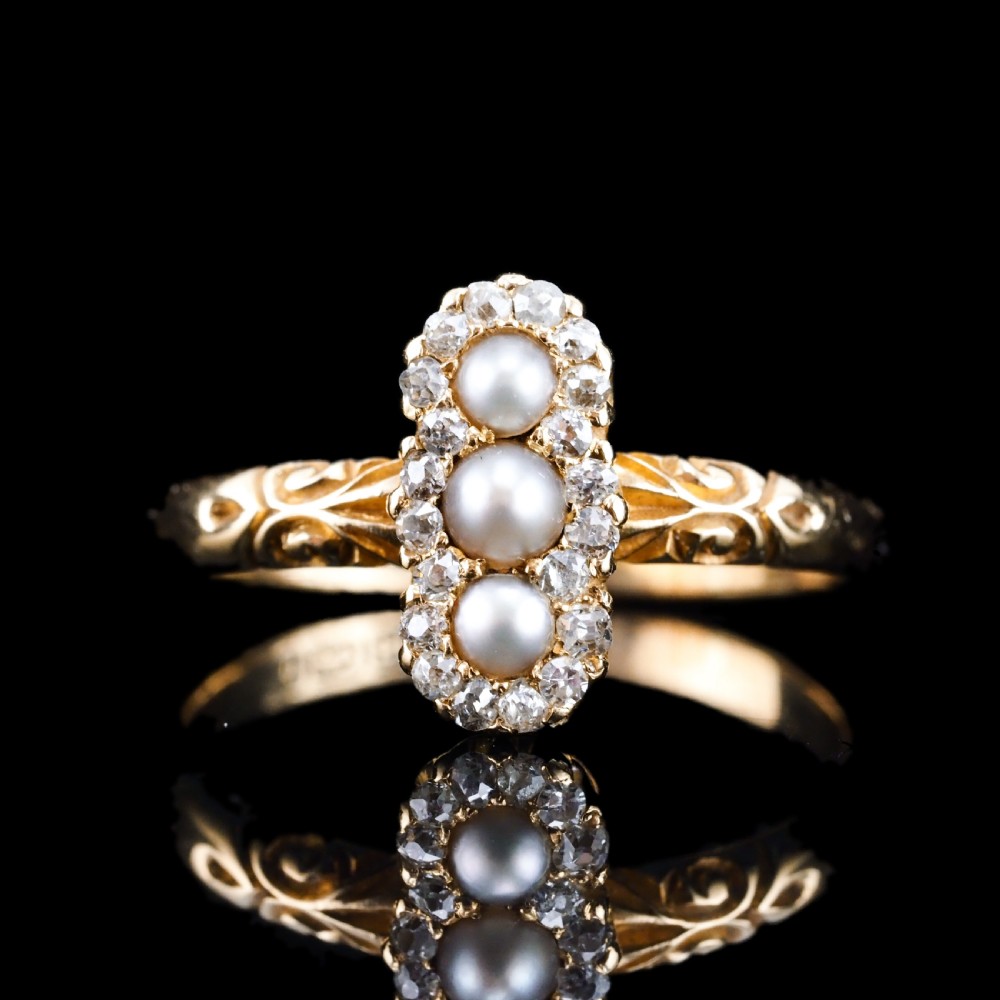 An 18 carat yellow gold ring featuring a vertical triple cluster set with three central pearls surrounded by small diamonds, complete with carved detail on the shoulders. View VI