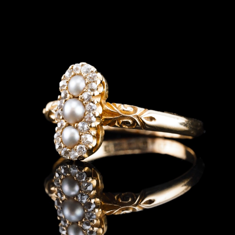 An 18 carat yellow gold ring featuring a vertical triple cluster set with three central pearls surrounded by small diamonds, complete with carved detail on the shoulders. View X