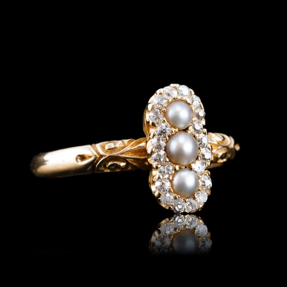 An 18 carat yellow gold ring featuring a vertical triple cluster set with three central pearls surrounded by small diamonds, complete with carved detail on the shoulders. View XI