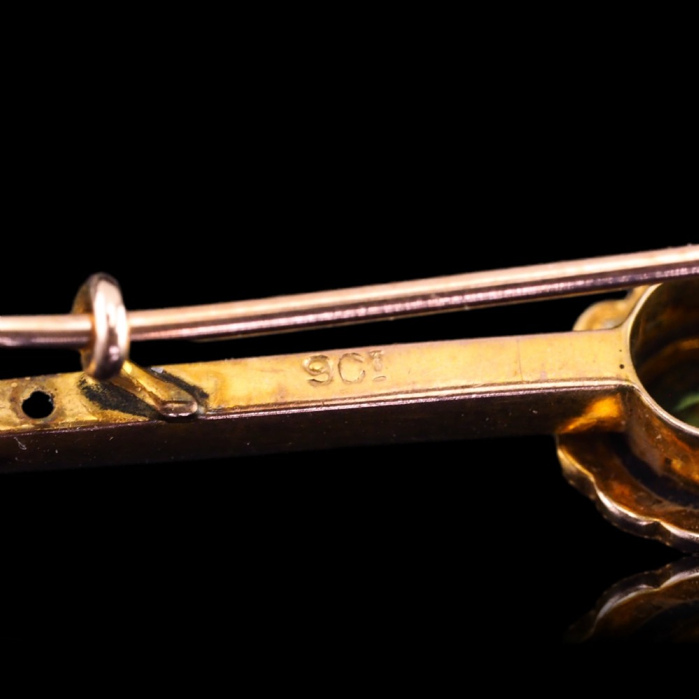 A 9ct gold late Victorian bar brooch featuring a central round faceted green peridot framed by a seed pearl halo, extending into pearl-set horizontal bars. View II