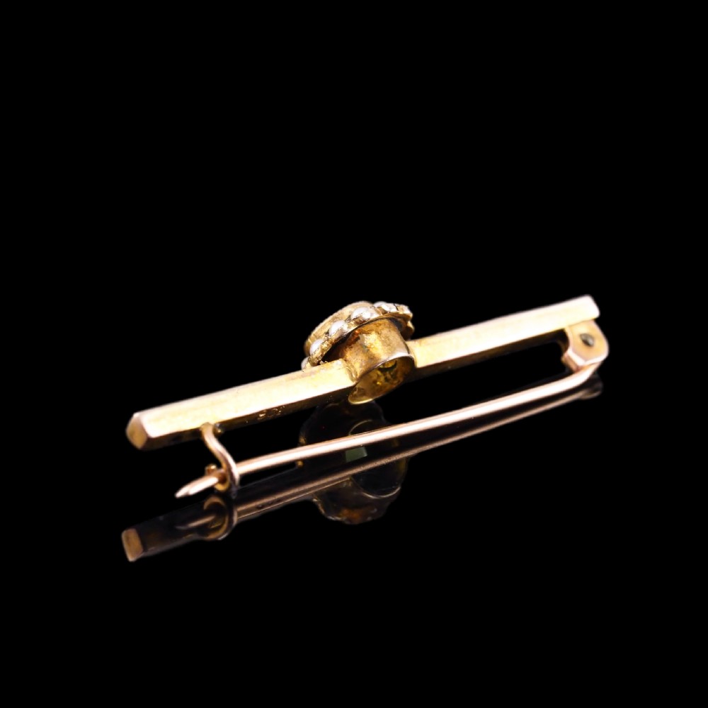 A 9ct gold late Victorian bar brooch featuring a central round faceted green peridot framed by a seed pearl halo, extending into pearl-set horizontal bars. View III