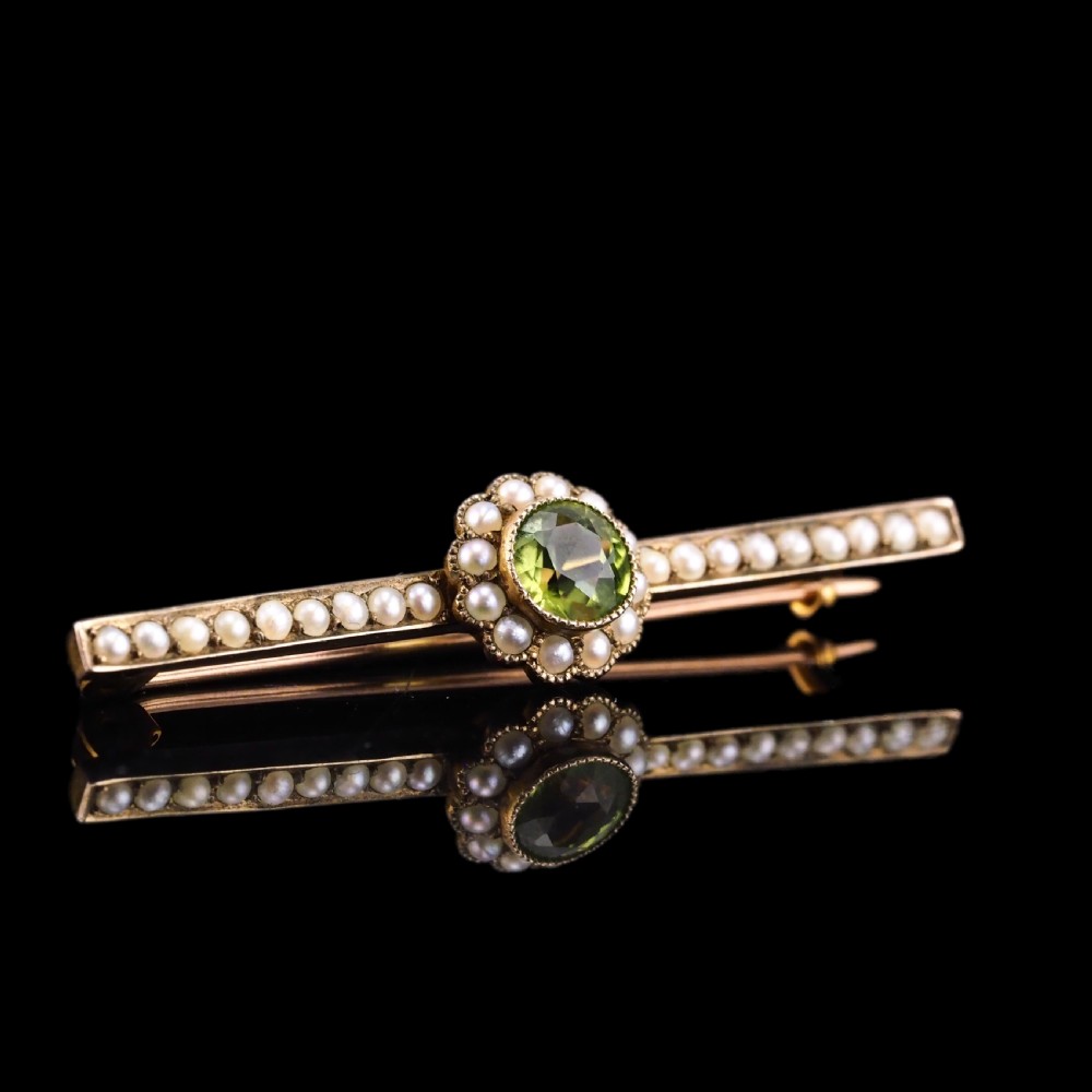 A 9ct gold late Victorian bar brooch featuring a central round faceted green peridot framed by a seed pearl halo, extending into pearl-set horizontal bars. View VIII