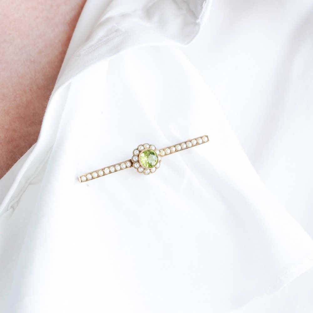 A 9ct gold late Victorian bar brooch featuring a central round faceted green peridot framed by a seed pearl halo, extending into pearl-set horizontal bars. View XI