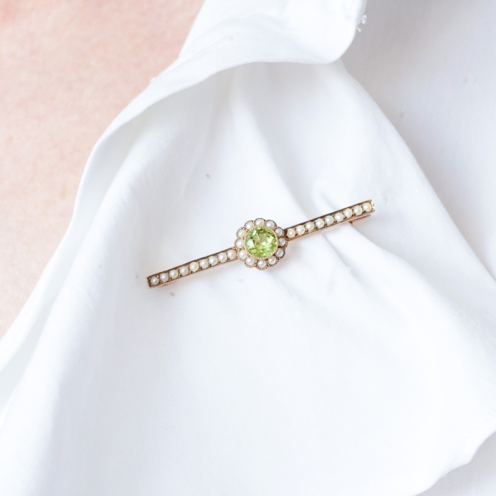 A 9ct gold late Victorian bar brooch featuring a central round faceted green peridot framed by a seed pearl halo, extending into pearl-set horizontal bars. View XIII