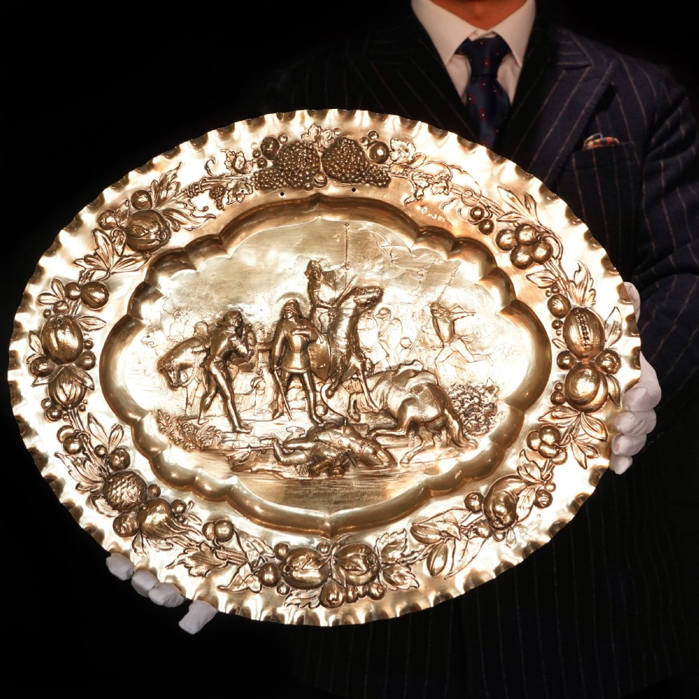 An oval 19th-century solid silver gilt charger dish featuring a central raised relief of a battle scene surrounded by embossed fruit borders. View III