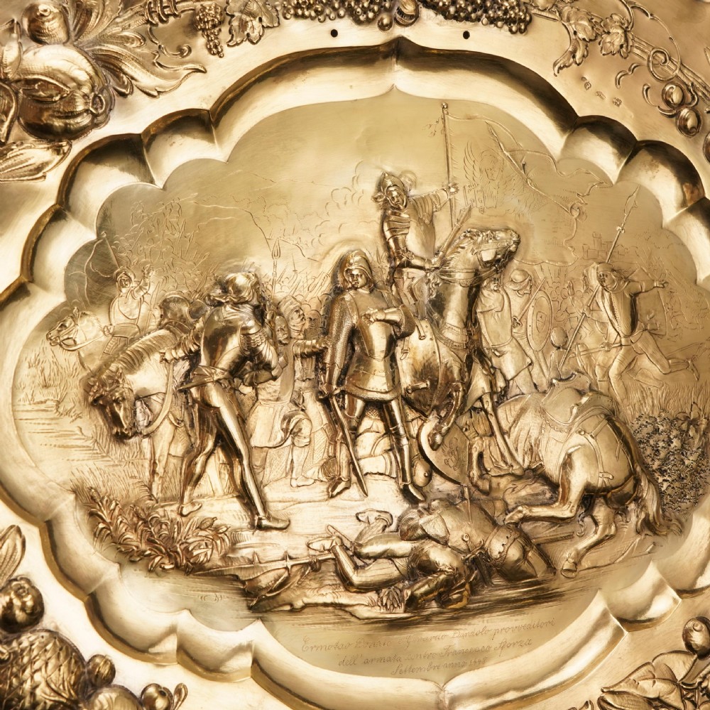 An oval 19th-century solid silver gilt charger dish featuring a central raised relief of a battle scene surrounded by embossed fruit borders. View VI
