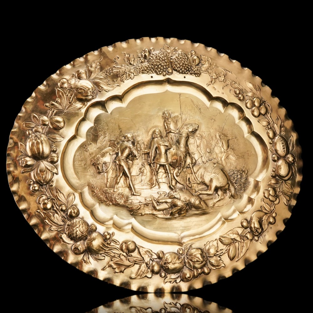 An oval 19th-century solid silver gilt charger dish featuring a central raised relief of a battle scene surrounded by embossed fruit borders. View VII