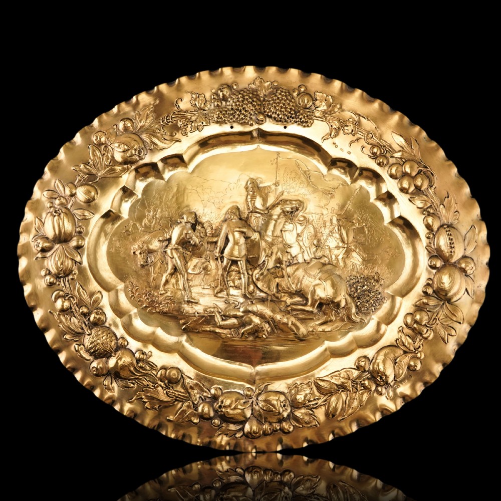 An oval 19th-century solid silver gilt charger dish featuring a central raised relief of a battle scene surrounded by embossed fruit borders. View IX