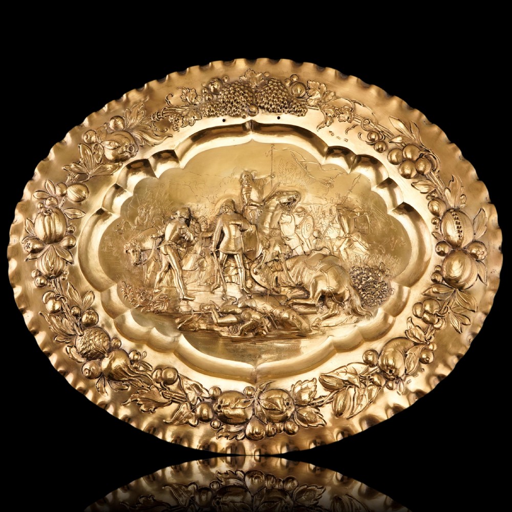 An oval 19th-century solid silver gilt charger dish featuring a central raised relief of a battle scene surrounded by embossed fruit borders. View XI