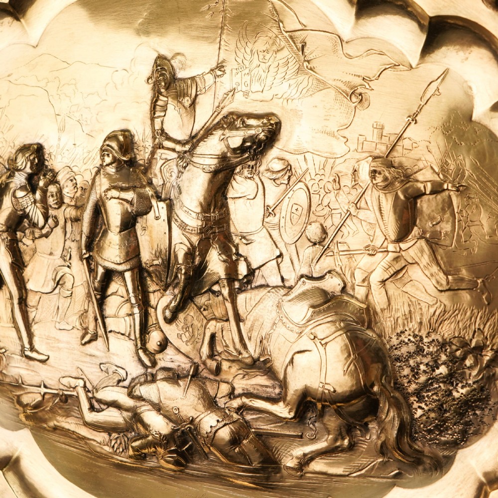 An oval 19th-century solid silver gilt charger dish featuring a central raised relief of a battle scene surrounded by embossed fruit borders. View XII