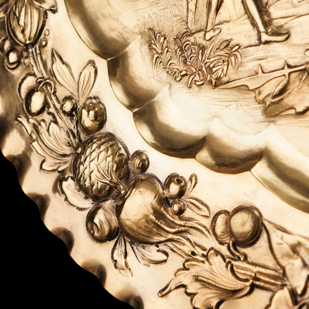 An oval 19th-century solid silver gilt charger dish featuring a central raised relief of a battle scene surrounded by embossed fruit borders. View XIII