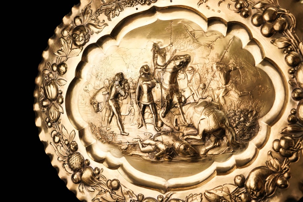 An oval 19th-century solid silver gilt charger dish featuring a central raised relief of a battle scene surrounded by embossed fruit borders. View XV