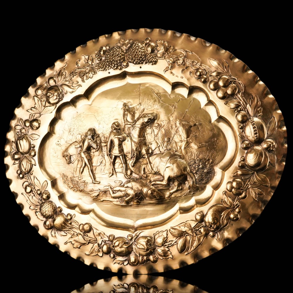 An oval 19th-century solid silver gilt charger dish featuring a central raised relief of a battle scene surrounded by embossed fruit borders. View XVI