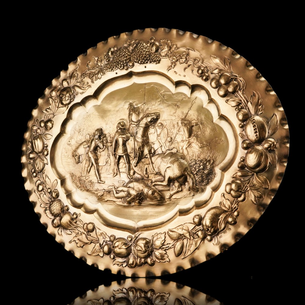 An oval 19th-century solid silver gilt charger dish featuring a central raised relief of a battle scene surrounded by embossed fruit borders. View XVII