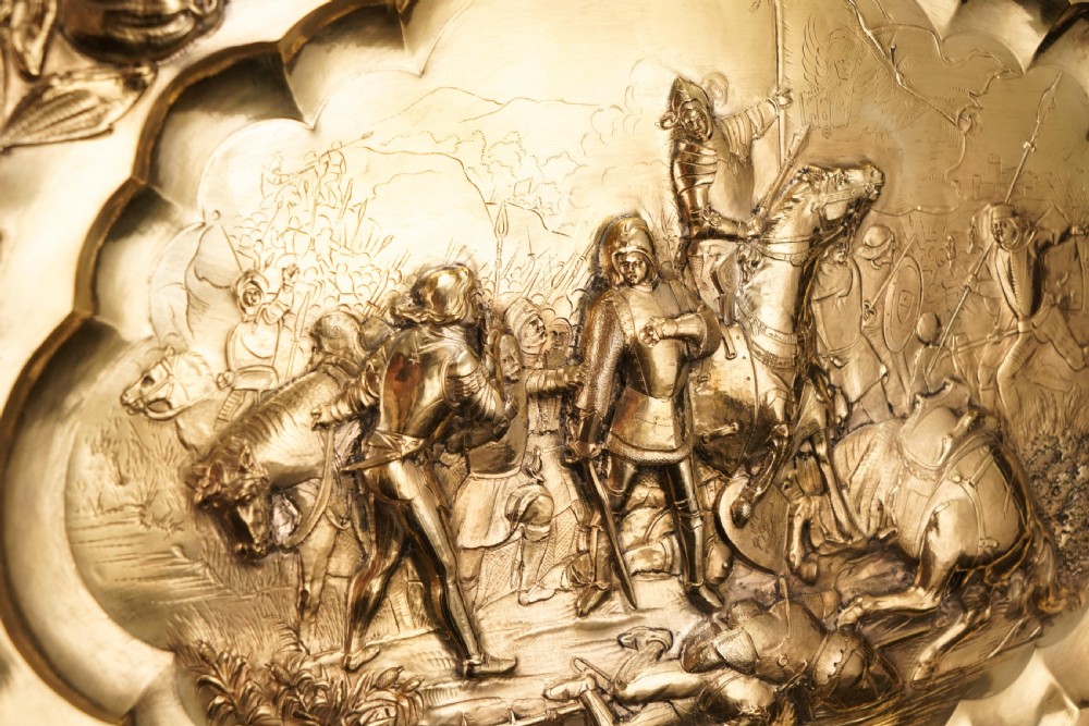 An oval 19th-century solid silver gilt charger dish featuring a central raised relief of a battle scene surrounded by embossed fruit borders. View XVIII