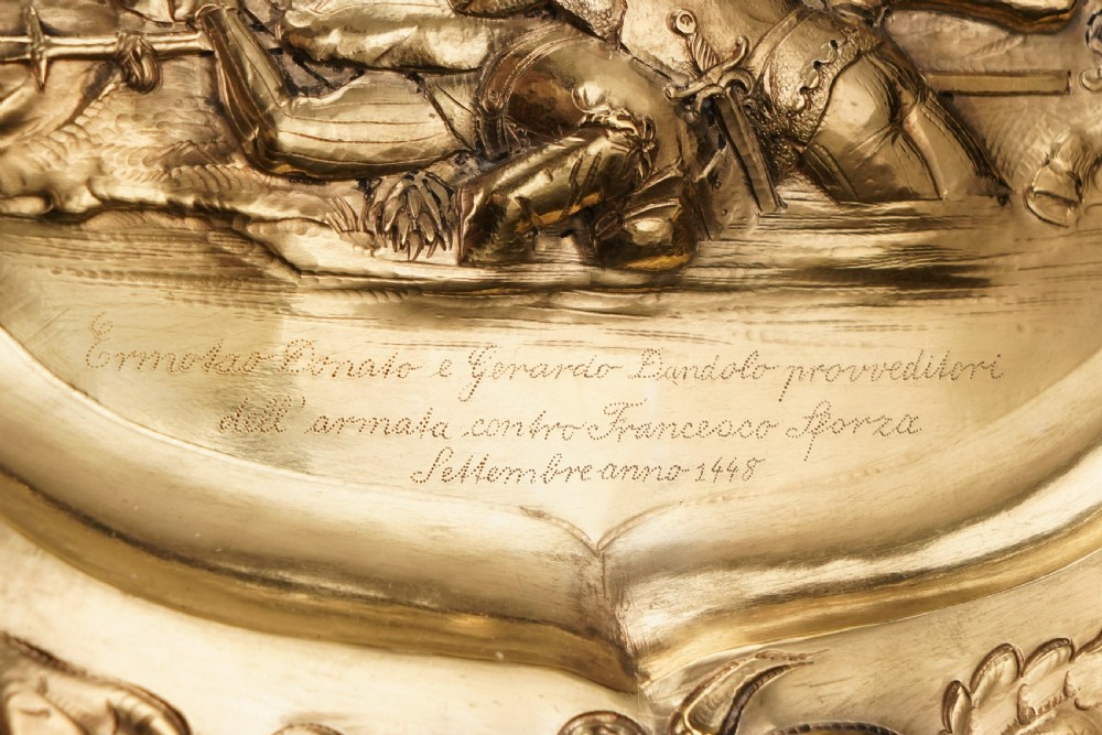 An oval 19th-century solid silver gilt charger dish featuring a central raised relief of a battle scene surrounded by embossed fruit borders. View XIX