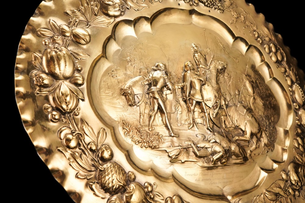 An oval 19th-century solid silver gilt charger dish featuring a central raised relief of a battle scene surrounded by embossed fruit borders. View XX